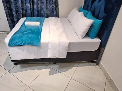 a bed with white sheets and blue pillows on it at Goshen Lodge Spencer in Cape Town