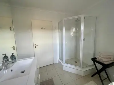 a white bathroom with a shower and a sink at Lakeview Cottage: Rural Retreat in Pampoenkraal