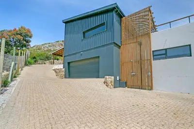 a house with a wooden door on a brick driveway at The Baydreamer, where the view soothes your soul in Pringle Bay