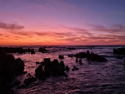 a sunset over the ocean with rocks in the water at The Baydreamer, where the view soothes your soul in Pringle Bay