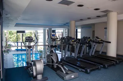 a gym with cardio machines and a swimming pool at Knightsbridge Superior Apartments in Cape Town