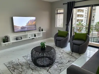 a living room with two chairs and a flat screen tv at Knightsbridge Superior Apartments in Cape Town