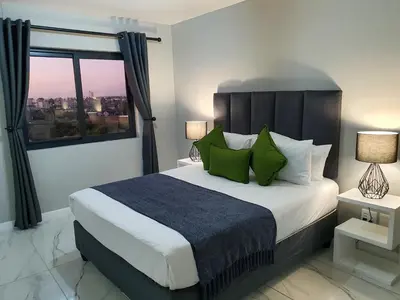 a bedroom with a bed with green pillows and a window at Knightsbridge Superior Apartments in Cape Town