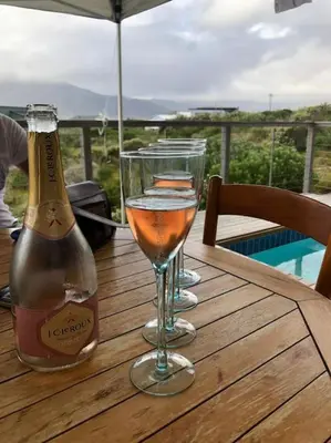 a bottle of champagne and two glasses on a wooden table at Secure, luxurious with lovely views in Pringle Bay