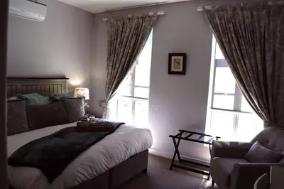 a bedroom with a bed and a chair and windows at Spacious, Modern & Convenient in Franschhoek