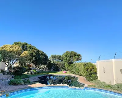 a swimming pool in front of a yard with trees at Whale Rock 25 in Hermanus