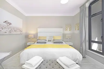 a white bedroom with a large bed with yellow and gray pillows at Witsand 804 in Bloubergstrand