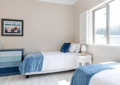 a bedroom with a bed and a dresser and a window at Seafront Retreat in Sandbaai in Hermanus