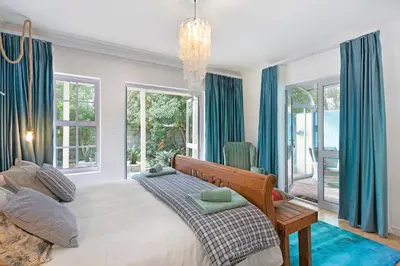 a bedroom with a large bed with blue curtains at Sunset Yellow Cottage in Cape Town