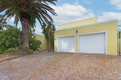a yellow building with two garage doors and a palm tree at Sunset Yellow Cottage in Cape Town