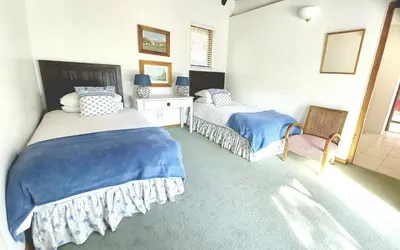 a bedroom with two beds and a chair at Grotto Cottage in Hermanus