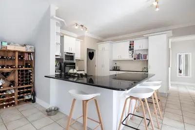 a kitchen with white cabinets and a black counter and stools at Sunset Villa 50 in Cape Town