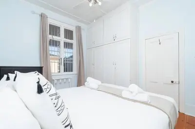 a white bedroom with two white beds and a window at Enchanting Abode in Rosebank in Cape Town