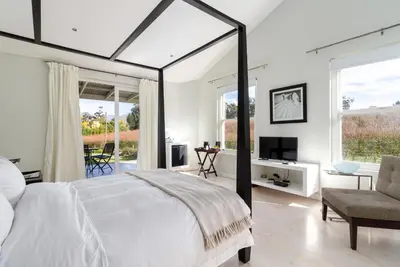 a white bedroom with a large bed and a tv at La Terra de Luc in Franschhoek