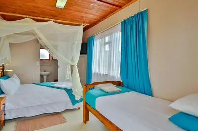 two beds in a bedroom with blue curtains at Fisherhaven Travellers Lodge in Hermanus