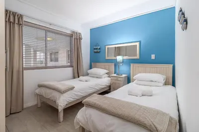 two beds in a room with blue walls at Luxury Beach Escape Sleeps 4 - Ocean View - Spa - Pool - Gym - Back Up Power in Cape Town