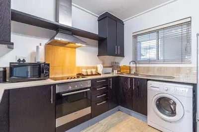 a kitchen with black cabinets and a washer and dryer at Luxury Beach Escape Sleeps 4 - Ocean View - Spa - Pool - Gym - Back Up Power in Cape Town