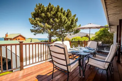 a wooden deck with a table with chairs and an umbrella at Klein Paradys in Kleinmond