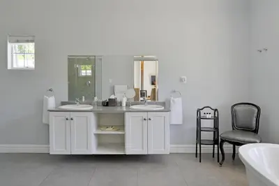 a white bathroom with two sinks and a chair at Fransvliet Guest House in Franschhoek