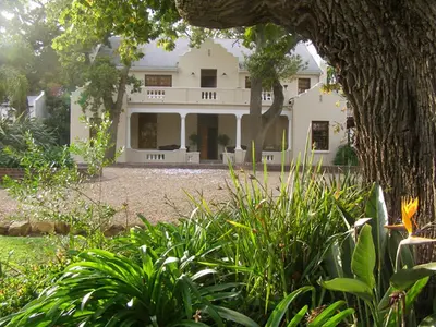 a large white house in the middle of a yard at Ongegund Lodge in Somerset West