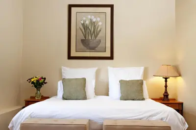 a bedroom with a white bed with a vase of flowers at Ongegund Lodge in Somerset West