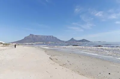 a person walking on a beach with a mountain in the background at 002 Burmeister on Park- 2 minute walk from the beach in Cape Town