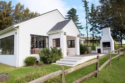 a white house with a wooden fence at High Season Farm Luxury Cottages in Hermanus