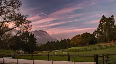 a field with a fence and a mountain in the background at High Season Farm Luxury Cottages in Hermanus