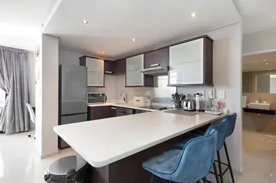 a kitchen with a white counter and blue chairs at Modern 3 Bed Apartment Blouberg in Cape Town