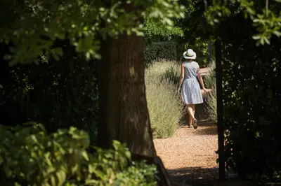 a woman in a hat walking down a path at La Clé Village in Franschhoek
