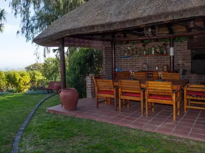 a patio with a table with chairs and a thatch roof at Villa Vista in Somerset West