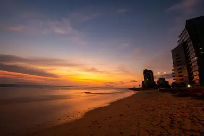 a sunset on a beach with buildings and the ocean at Ocean Breeze Hotel in Strand