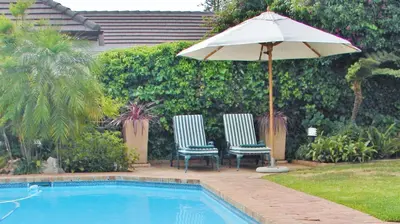 two chairs and an umbrella next to a swimming pool at Majorca House in Somerset West