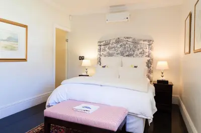 a bedroom with a large white bed and a pink bench at Auberge Daniella in Franschhoek