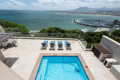 a swimming pool with chairs and a view of the ocean at 'Harbour Views' - 2 bedroom, sleeps 4 with private pool and large veranda! in Gordonʼs Bay