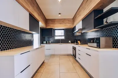 a kitchen with white cabinets and black tiles on the wall at Phoenix Home in Cape Town