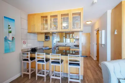 a kitchen with wooden cabinets and a bar with stools at Beachfront Luxury Apartment - Hibernian Towers 309 Strand - Self Catering in Cape Town