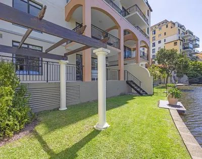 a house with columns and grass in front of the water at Capri On Lake 101 The Island Club in Cape Town