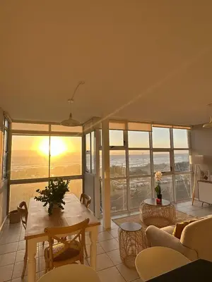 a living room with a table and a view of the ocean at Charming beachfront Strand apartment in Cape Town