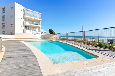 a swimming pool next to a building and the ocean at Lagoon Beach 29A in Cape Town