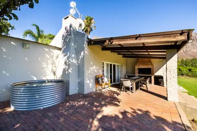 a patio with a table and chairs and a building at Dorpsig Cottage in Paarl