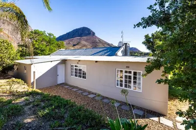 a white house with a mountain in the background at Dorpsig Cottage in Paarl