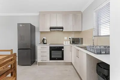 a kitchen with white cabinets and a stainless steel refrigerator at Elegant, Spotless 2 Bed For Enchanted Stays in Cape Town