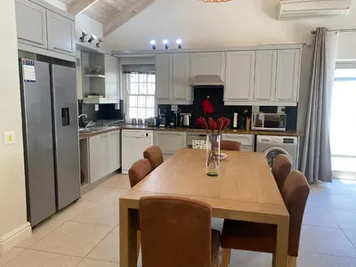 a kitchen with a wooden table with chairs and a refrigerator at Leopard Tree Cottage in Franschhoek
