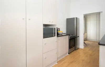 a white kitchen with white cabinets and a refrigerator at Middedorp Apartments in Stellenbosch