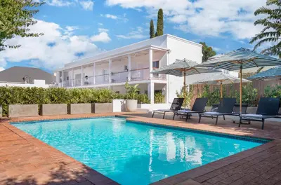 a swimming pool in front of a house with umbrellas at Middedorp Apartments in Stellenbosch