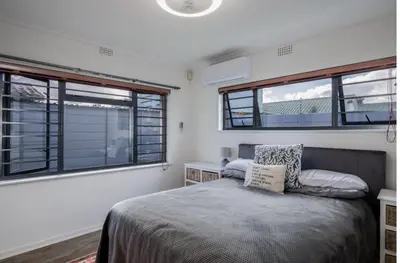 a bedroom with a bed and two windows at The Elephant Cottage in Cape Town
