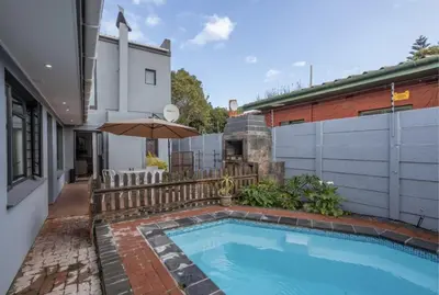 a swimming pool with an umbrella next to a building at The Elephant Cottage in Cape Town