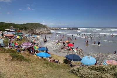 a crowd of people on a beach with umbrellas and the ocean at Casa Familia in Hermanus