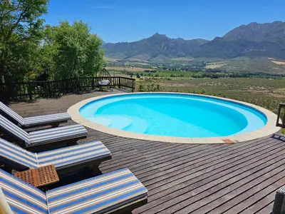 a swimming pool on a wooden deck with chairs and mountains at Valley View Eco Country Estate - Paradise in the Winelands in Villiersdorp